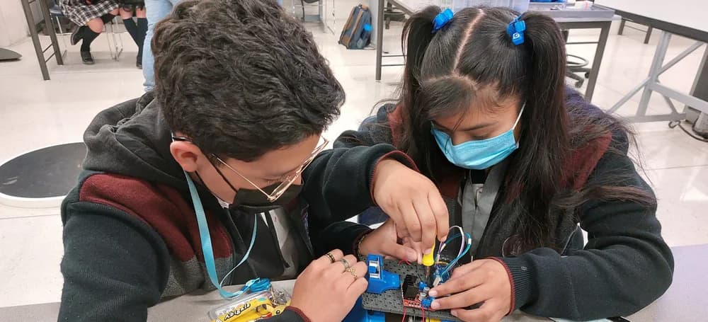 Dos estudiantes armando un pequeño robot con un desarmador