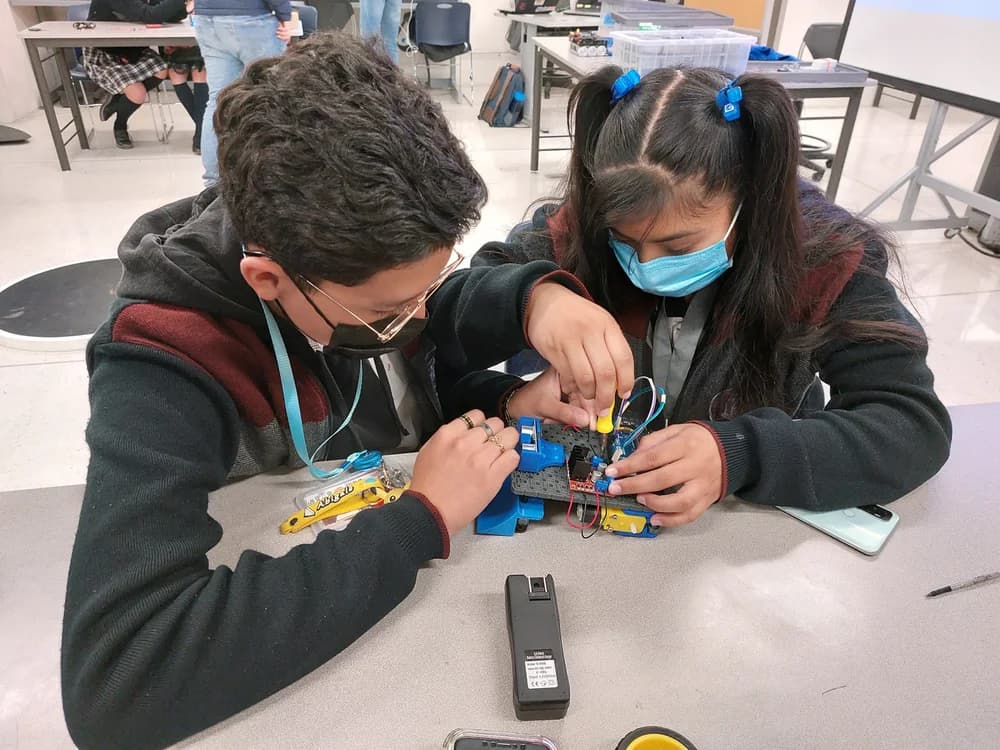 Dos estudiantes armando un pequeño robot con un desarmador